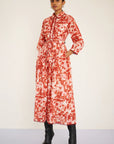 Woman wearing a red and white patterned dress with black boots on a plain background