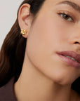Close-up of a person wearing gold earrings with a neutral background