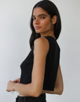 Woman wearing a black sleeveless top against a white background, back view