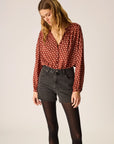 Woman wearing a red polka dot blouse and black jeans on a plain background