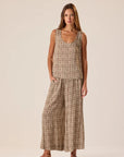 A woman modeling a sleeveless, wide-leg two-piece set in a brown and beige houndstooth pattern, standing against a solid light beige studio background.