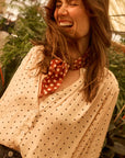 Woman laughing with a polka dot scarf around her neck, surrounded by greenery.