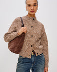 Woman wearing a brown patterned cardigan and blue jeans, holding a brown bag against a white background