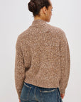Person wearing a brown patterned sweater and blue jeans on a white background