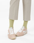 Person wearing checkered pants, light green socks, and pink sneakers on a white background