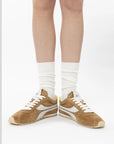 Tan sneakers with white laces worn with white socks on a plain background