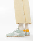 Light green sneakers worn with beige pants and white socks on a white background