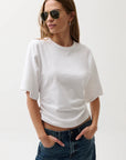 Woman wearing a white t-shirt and blue jeans with sunglasses on a plain background