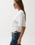 Woman wearing a white t-shirt and blue jeans against a plain background