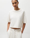 Person wearing a white crop top and light-colored pants on a plain background