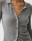 A close-up of a person wearing a gray ribbed long-sleeve button-up shirt with a pointed collar and white buttons.