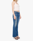 A woman modeling a pair of medium-wash blue flare jeans with a white ribbed crop top and sunglasses, standing against a plain white background.