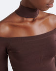 Close-up of a model wearing a dark brown ribbed off-the-shoulder top with a matching high ribbed collar against a light gray background.