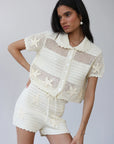 Woman wearing a cream-colored crochet outfit on a plain background