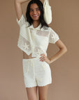 Woman wearing a white crochet outfit holding a matching bag against a beige background