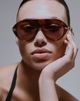 model wearing tortoise sunglasses with gold accents on a grey background
