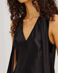 Close up of woman wearing a black satin top and black pants against a plain background