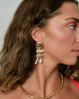 Close-up of a woman wearing gold earrings and a gold necklace against a neutral background