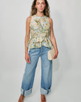 Woman wearing a floral sleeveless top and blue jeans against a plain background, full body front
