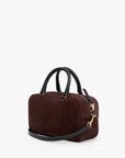 A dark brown suede handbag with black leather handles and a matching shoulder strap, accented by gold-tone hardware, shown against a plain white background.