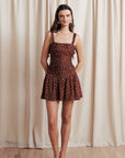 Woman wearing a brown polka dot dress against a beige curtain background