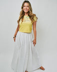 Woman wearing a yellow top and white skirt on a plain background