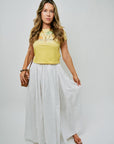 Woman wearing a yellow top and white skirt on a plain background, full body front