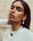 Woman wearing a necklace and earrings against a textured wall.