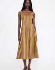 A model wearing a sleeveless midi dress with vertical mustard yellow and brown stripes, paired with tan pointed-toe flats, against a plain white studio background.