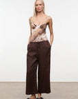 Woman wearing a patterned top and brown wide-leg pants against a white background