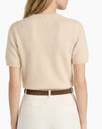 Woman wearing a beige sweater and white pants with a brown belt on a white background