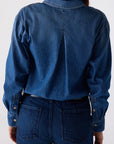 A person shown from the back wearing a dark blue denim long-sleeve button-up shirt and matching dark blue denim jeans against a plain light gray studio background.