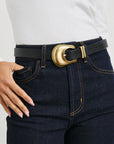 Dark blue jeans with a gold belt buckle worn by a person on a light gray background