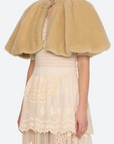 A model wearing a beige fuzzy cropped cape over a cream lace dress, photographed against a light gray studio background.