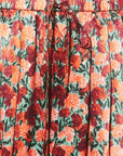 Close-up of a pleated skirt with an orange, red, and green floral print and a matching drawstring waist.