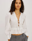 Woman wearing a white blouse with a deep neckline and gray pants on a light gray background