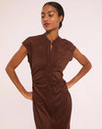 A woman modeling a sleeveless, button-front brown dress with a mock neck and gathered waist details, posed against a plain light background.