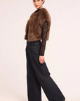 A model is shown from the side wearing a brown faux fur vest over a dark brown lace long-sleeve top, paired with dark wide-leg jeans and black pointed-toe heels, against a plain light background.