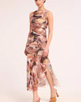 A model wearing a sleeveless, high-neck, ruched midi set with an abstract painterly print in shades of brown, beige, and pink, paired with tan platform heels, against a solid off-white background.