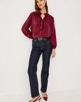 Woman wearing a burgundy blouse and dark jeans on a white background