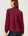 Person wearing a burgundy blouse and dark jeans on a white background