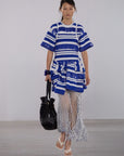 Model wearing a blue and white striped dress with a black handbag on a plain background