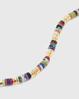 A close-up of a beaded strand, featuring a mix of colorful stone discs and textured gold spacer beads, set against a solid light gray background.