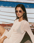 Woman wearing sunglasses and a beige sweater sitting on a wooden boat.