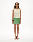 Woman wearing a white sleeveless top and green skirt on a white background