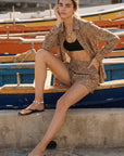 Woman in a patterned outfit sitting on a boat dock with boats in the background