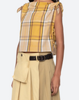 Woman wearing a yellow plaid top and beige pants on a white background