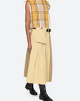 Woman wearing a yellow plaid top and beige skirt with a white background