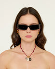 Woman wearing black sunglasses and a red necklace with shell pendants on a white background