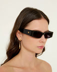 Woman wearing black sunglasses with a gold earring on a plain background